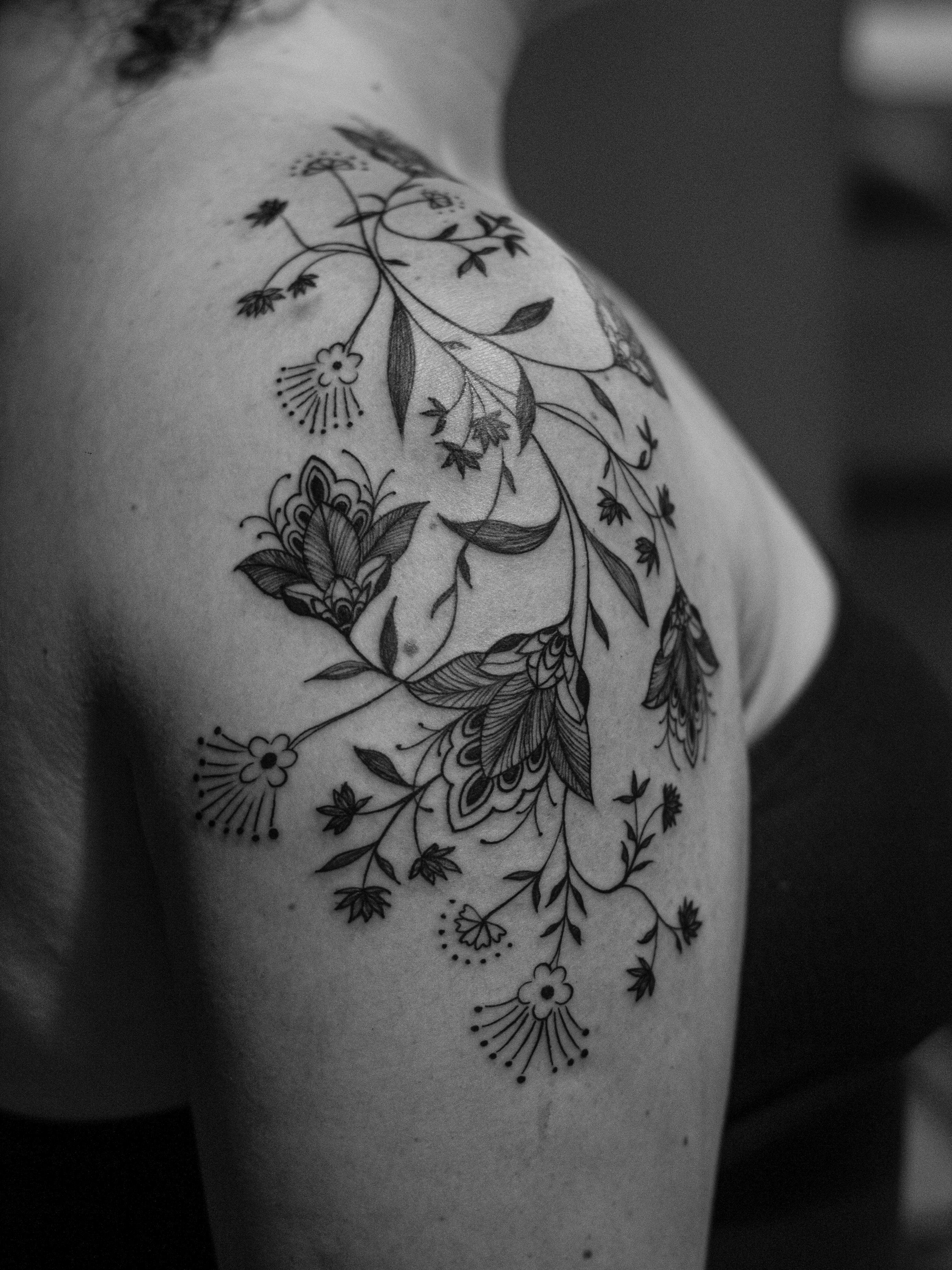 Ornamental tattoo made in fineline, on the shoulder and arm area, only in black (blackwork), representing ornaments and mandala flowers.