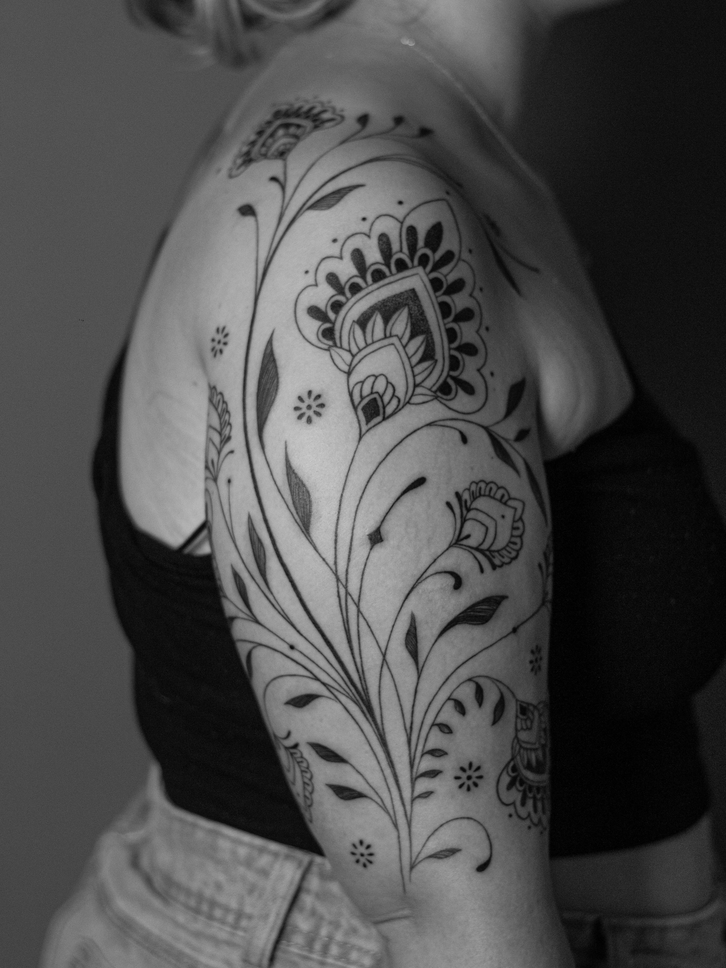 Ornamental tattoo made in fineline, only in black (blackwork), on the shoulder and arm area, representing ornaments and mandala flowers.