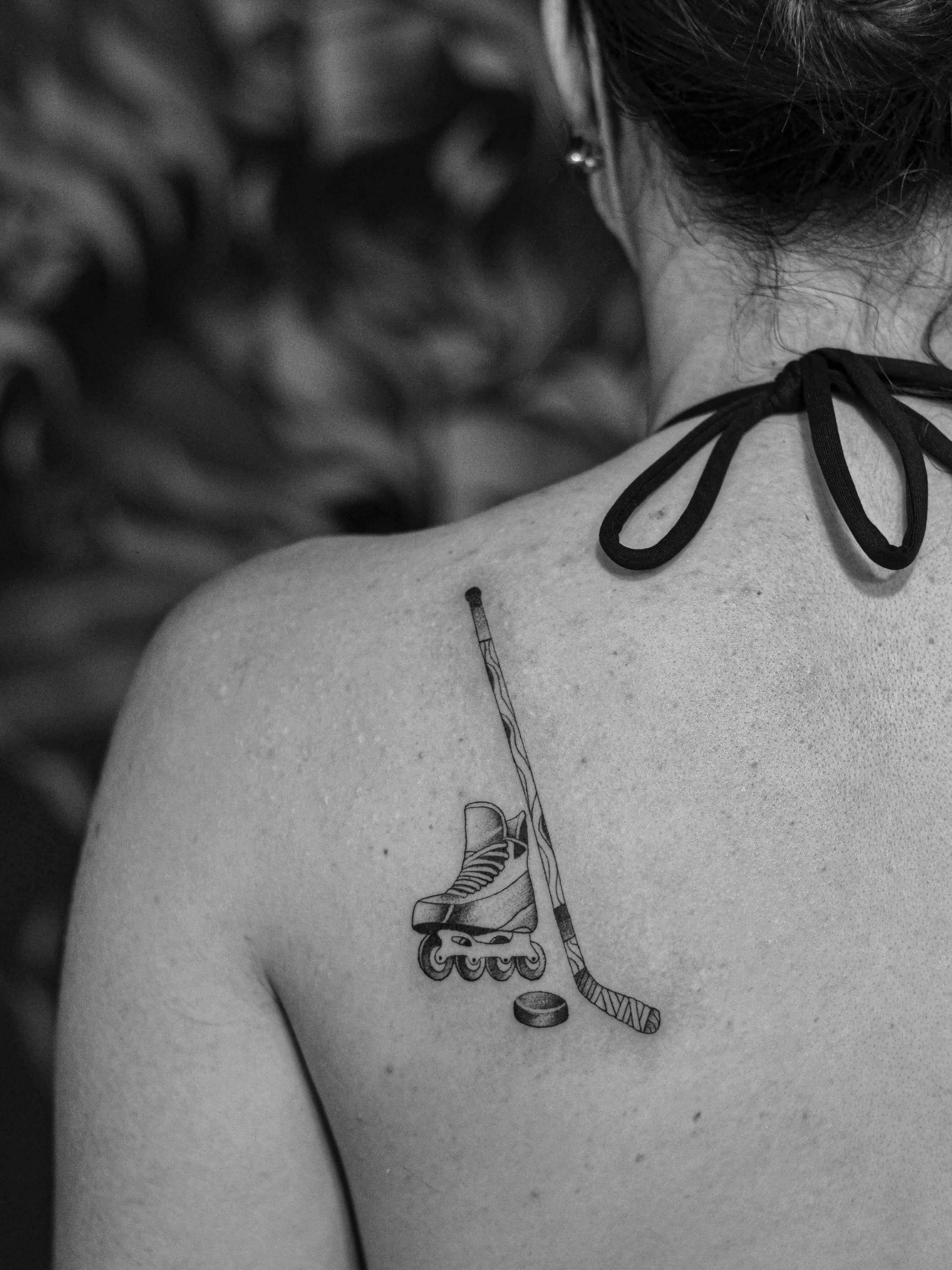 Minimalist tattoo made in fineline on the scapula area, representing hockey game equipment.