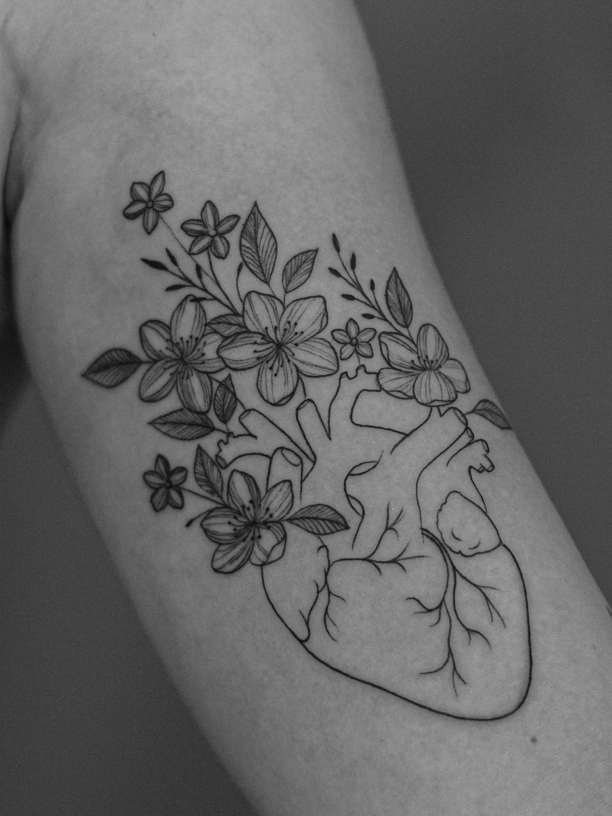 Minimalist tattoo made in fineline on the biceps area, representing a human heart, with flowers coming out of the heart's veins and arteries.