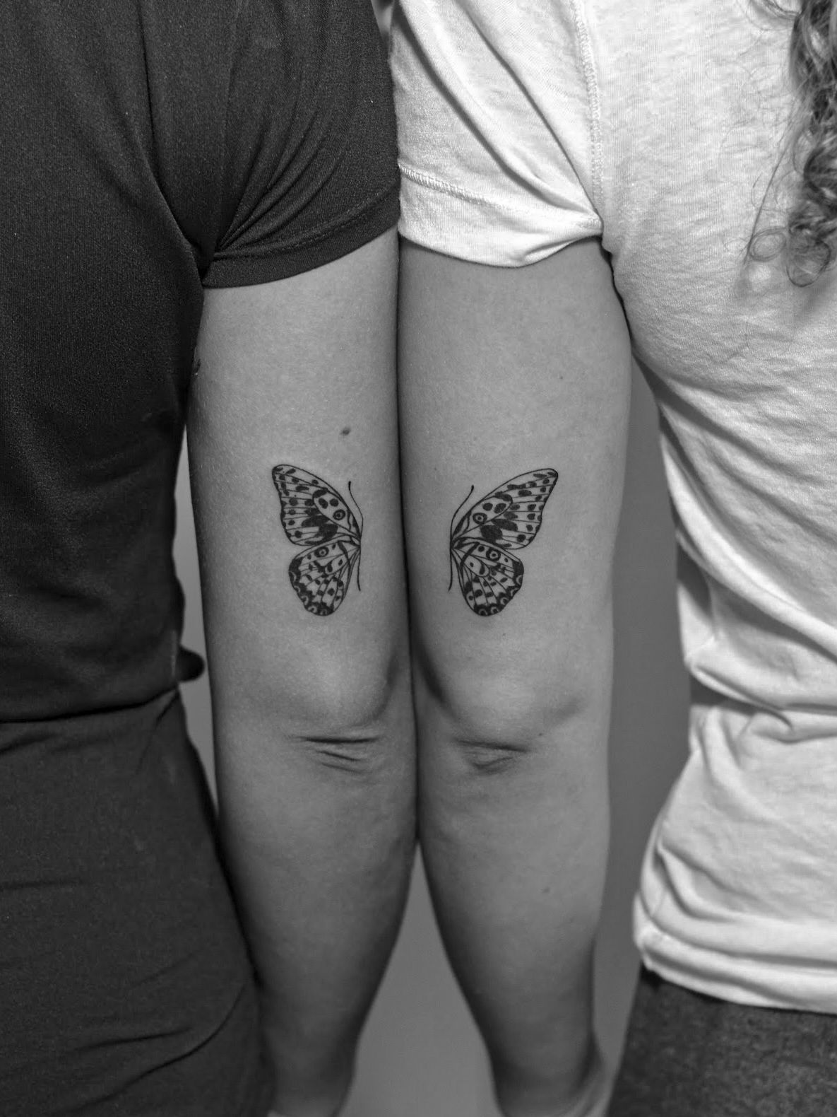 Minimalist tattoo made in fineline on the arm area, above the elbow, on two sisters, where each tattooed half of a butterfly.