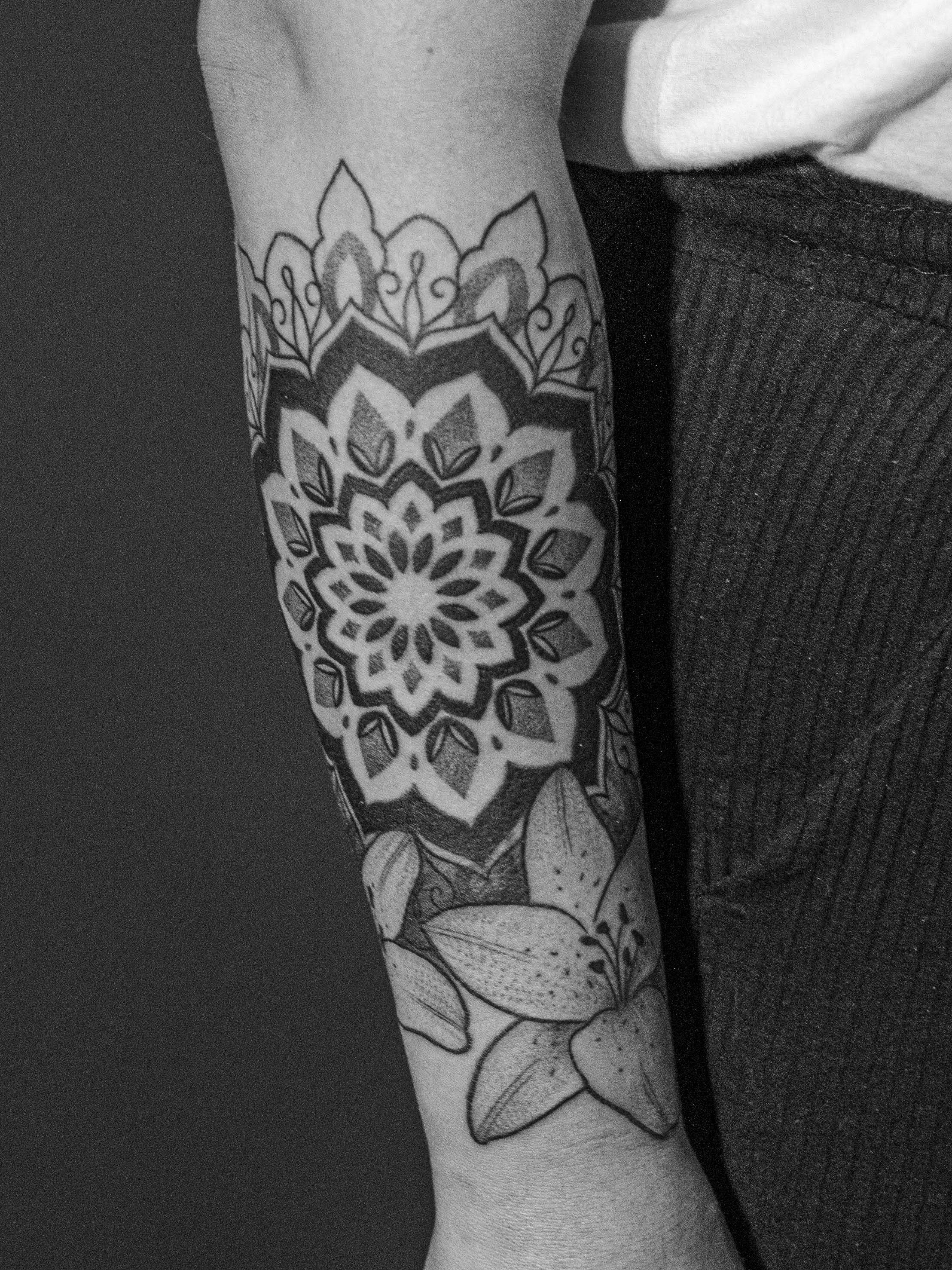 Tattoo made in dotwork on the forearm area, representing a flower/mandala and with two additional lilies.