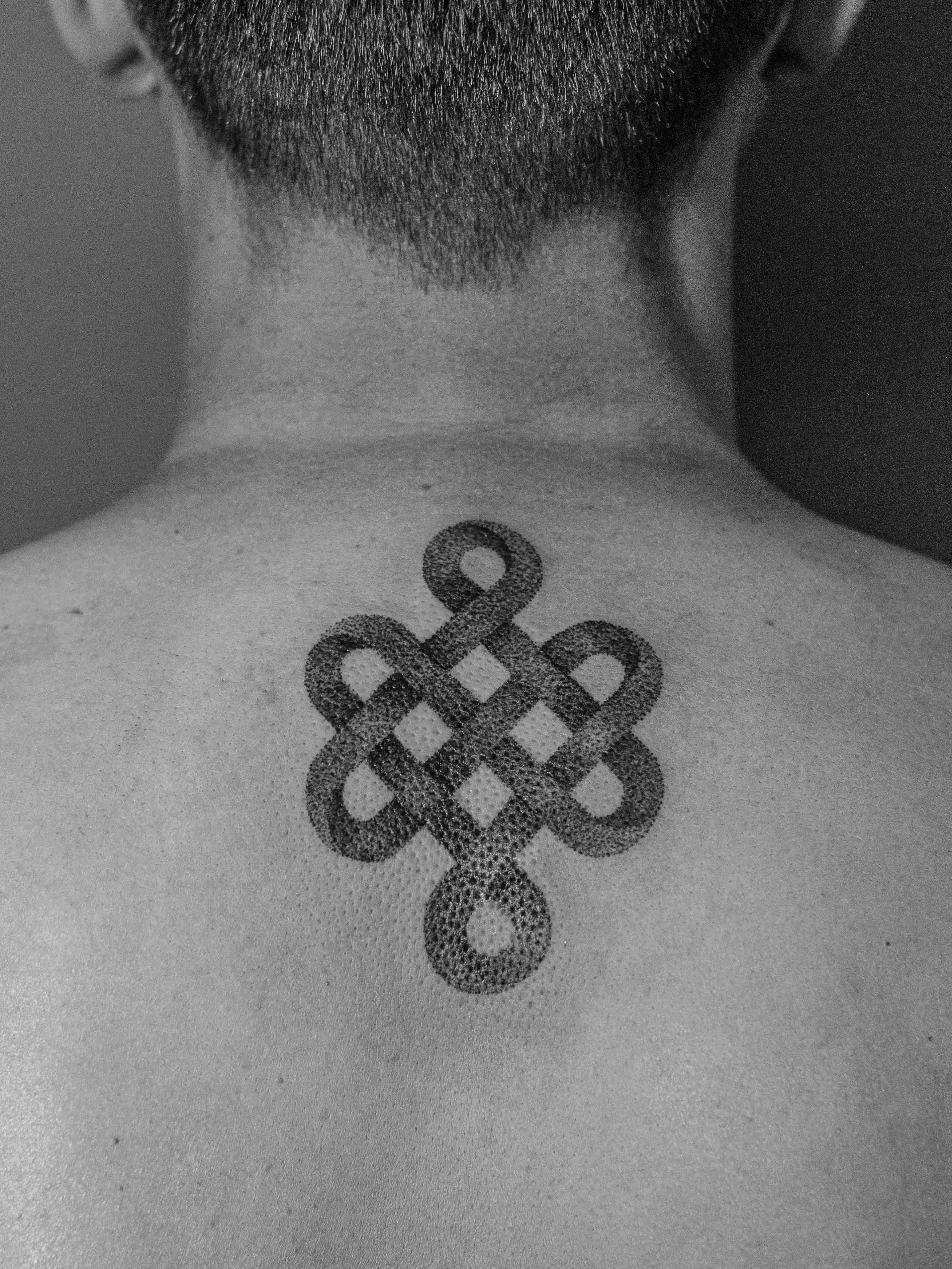 Minimalist tattoo made in dotwork on the back area, near the neck, representing the Buddhist symbol "endless knot".