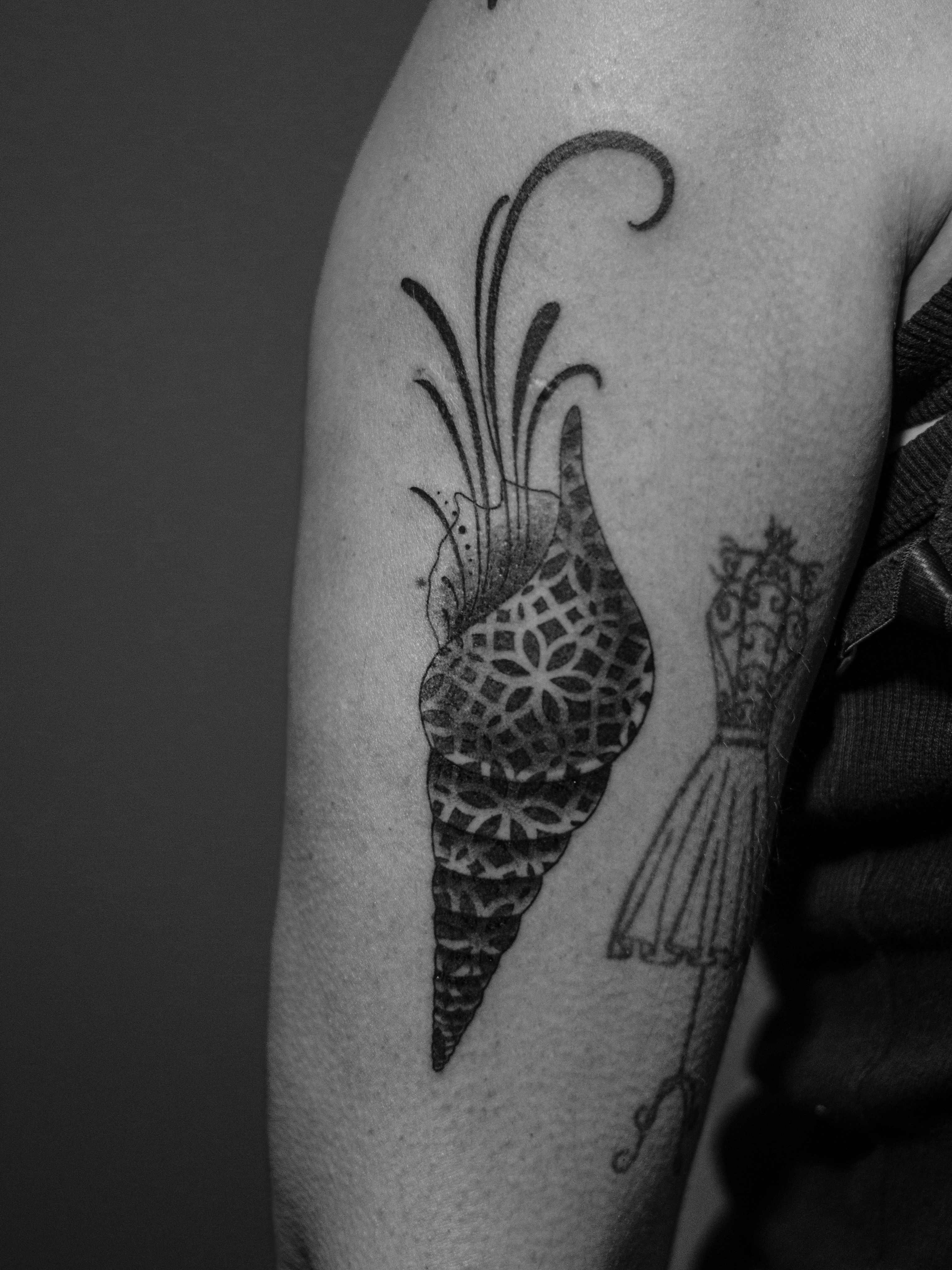 Minimalist tattoo made in dotwork on the arm area, representing a seashell, filled with geometric patterns.