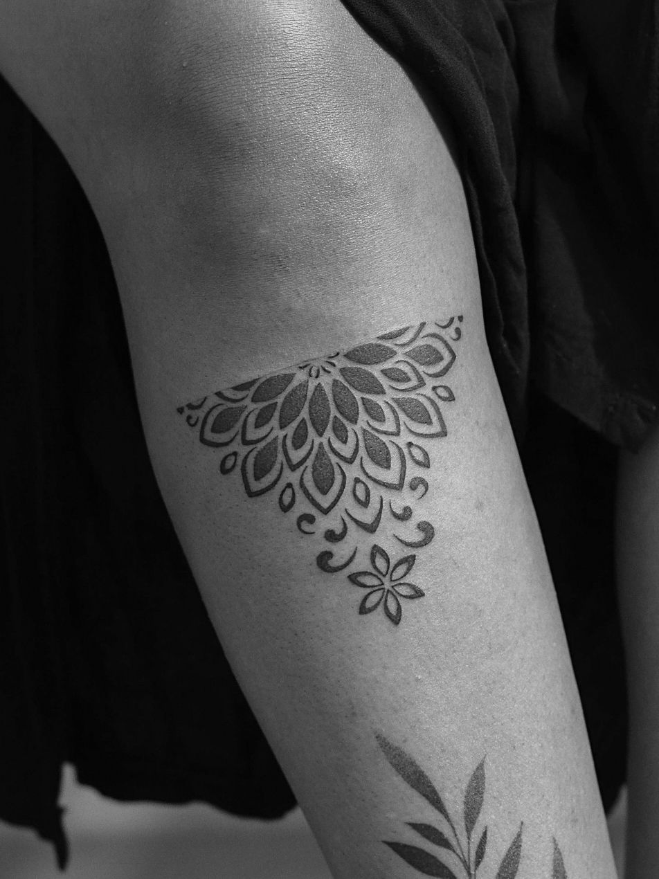 Minimalist tattoo made in dotwork on the leg, near the knee, representing half of a mandala.