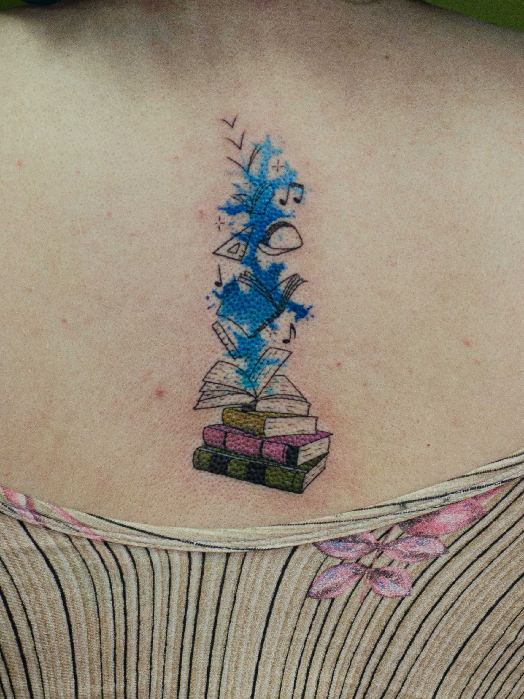 Minimalist tattoo made in fineline, colored, watercolor style, representing a stack of books, "exploding symbols and blue color", symbolizing absorbed knowledge.