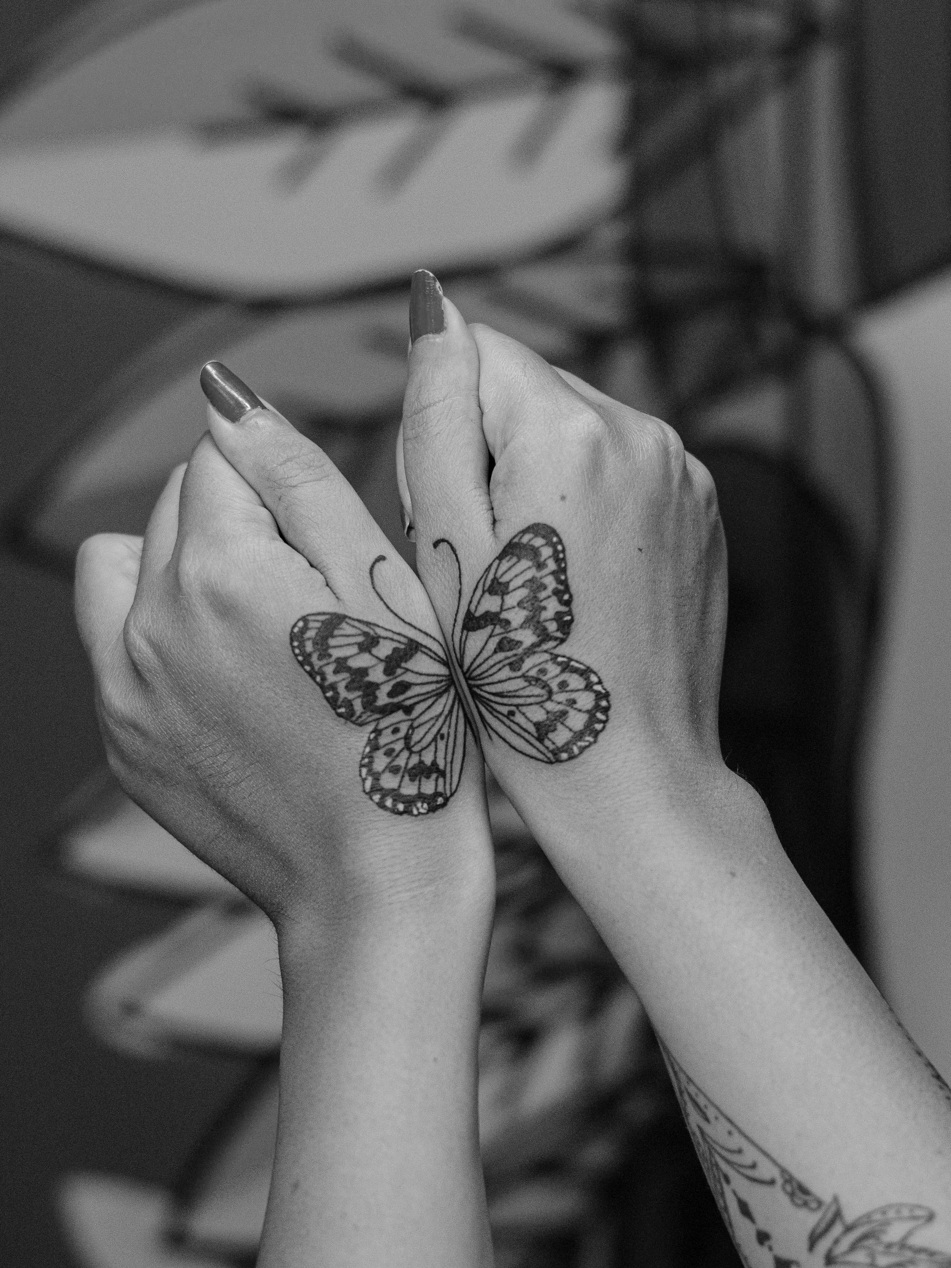 Minimalist tattoo, made in fineline, only in black (blackwork), on the thumbs area, representing a butterfly.