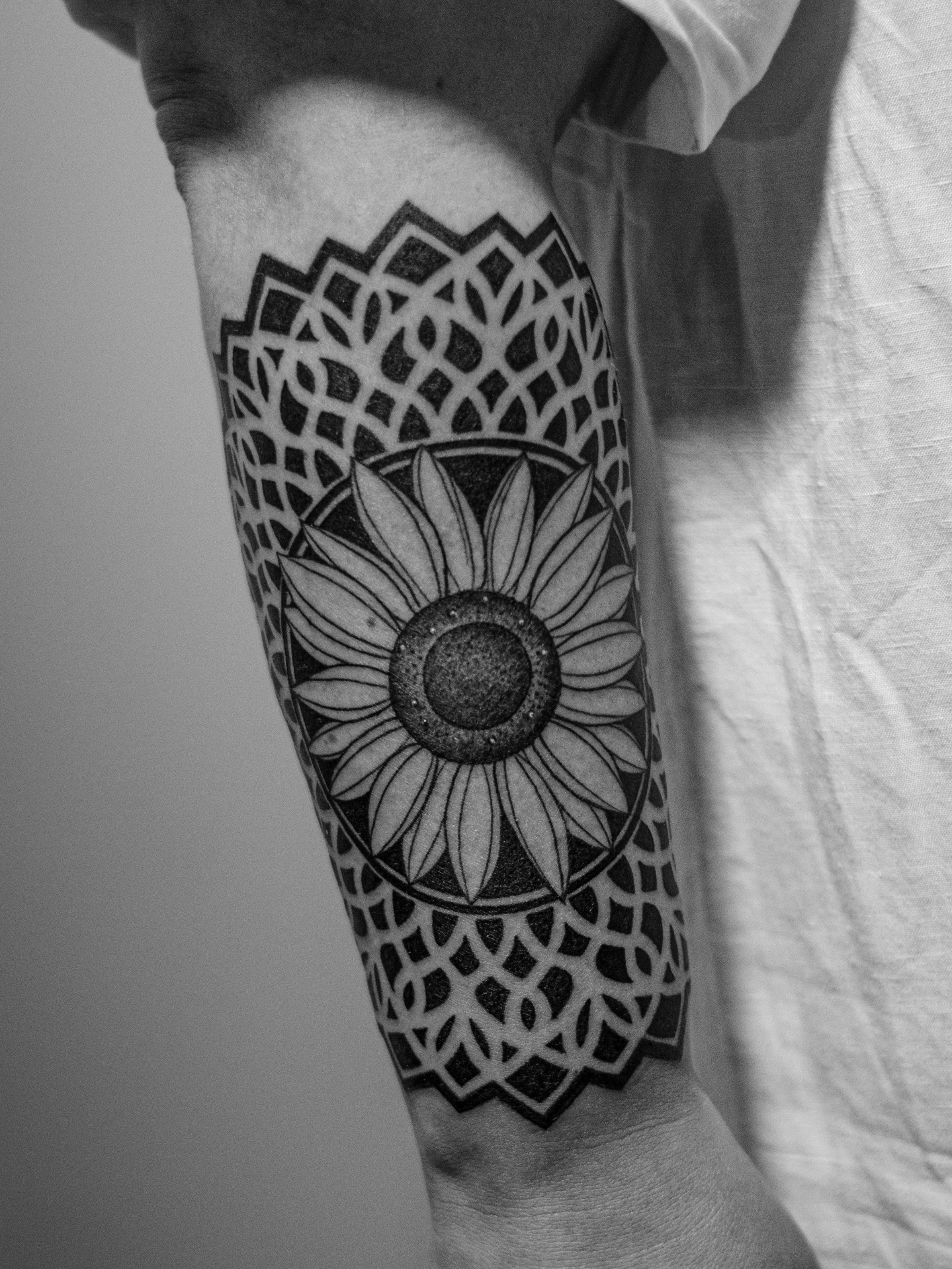 Geometric tattoo, made in dotwork, only in black (blackwork), on the forearm area, representing a mandala with a sunflower in the center.