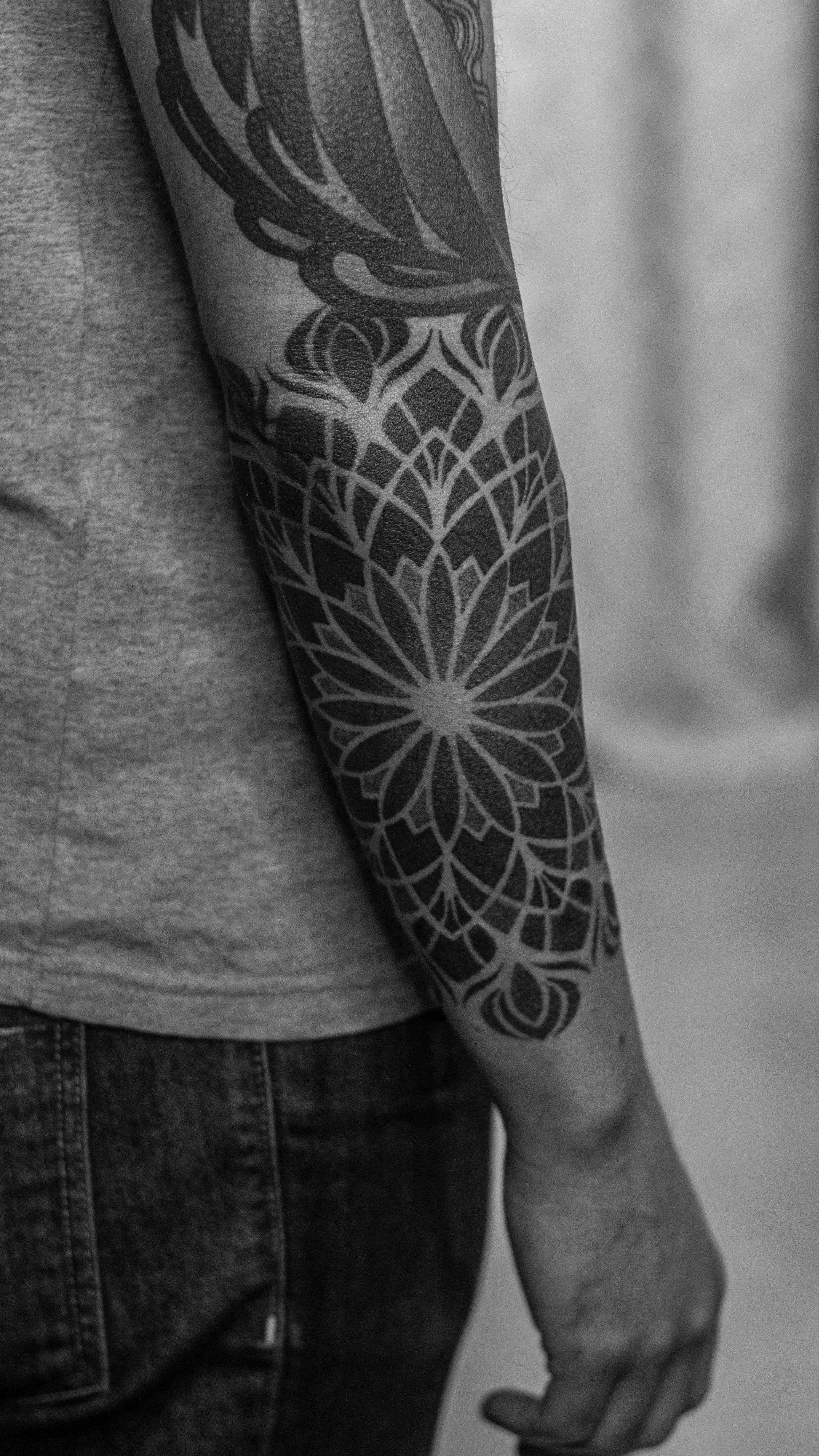 Geometric mandala in pointillism, defined by precise lines and solid fills that create a stark contrast between light and shadow. The flower-like composition expands across the forearm, conveying balance, symmetry, and visual strength.