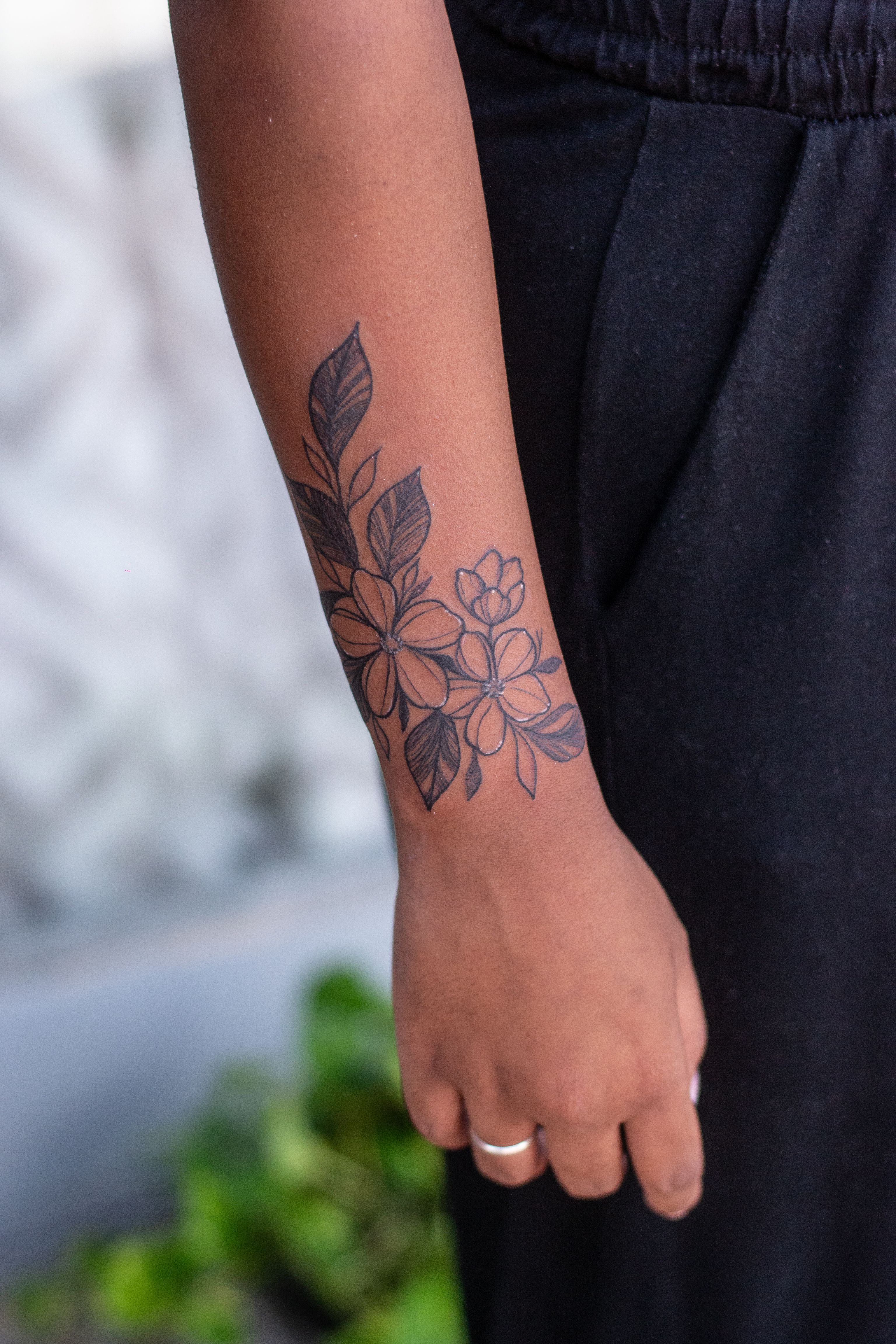 Floral tattoo in thin lines on the forearm near the wrist.